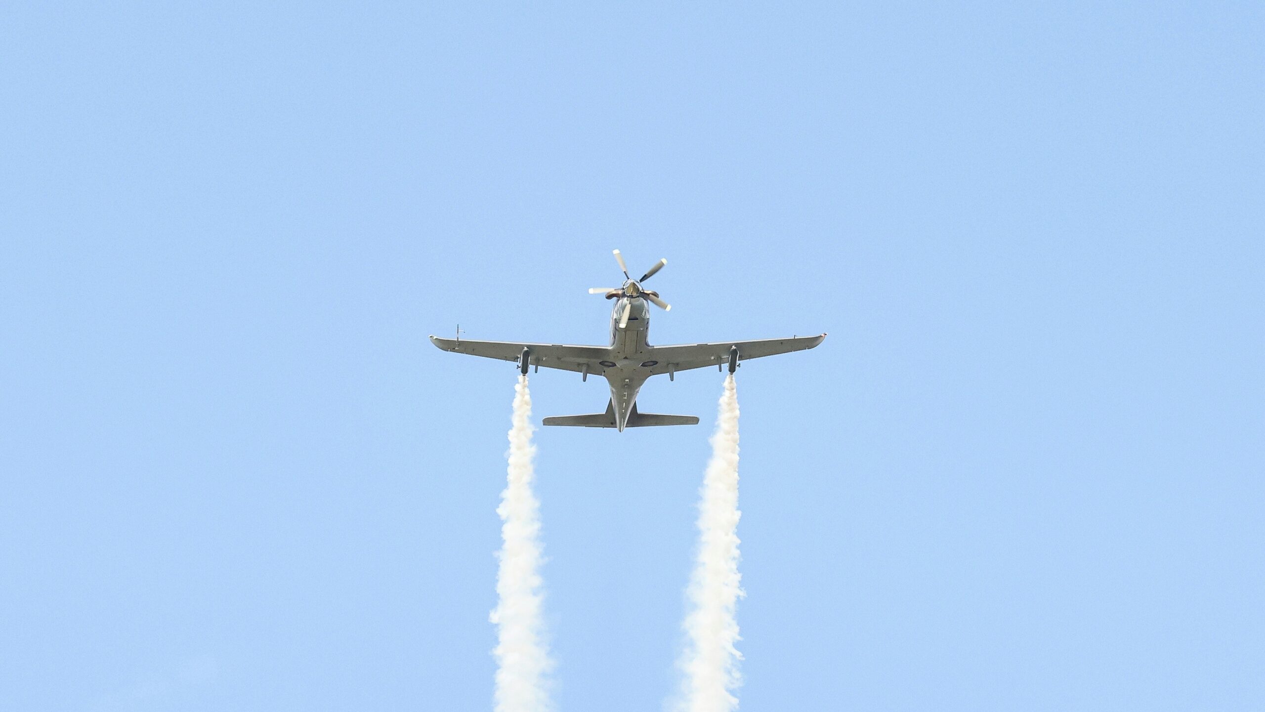 A plane flying in the air with two smoke trails behind it