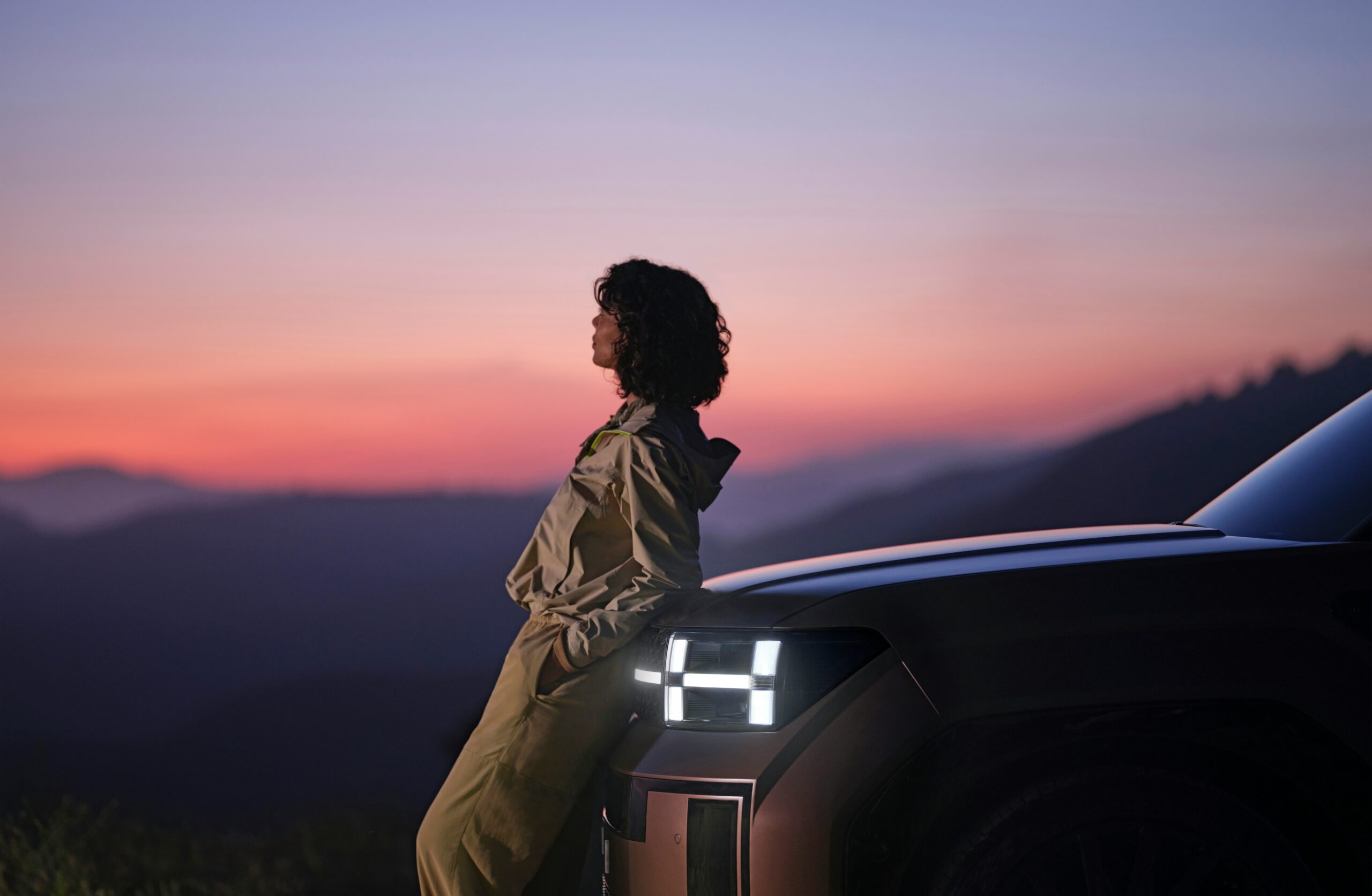 The Future of Transportation: Embracing Electric Vehicles and Moving Away from Gasoline a woman sitting on the hood of a car